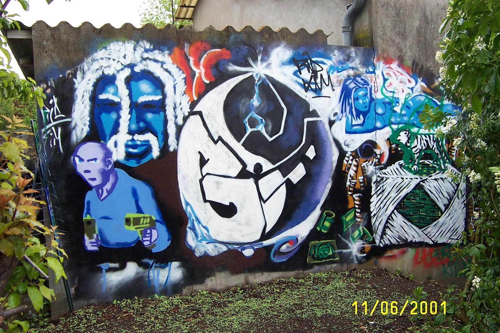 Une fresque graffiti sur un mur extérieur : des visages bleus, un personnage et un grand symbole rond.