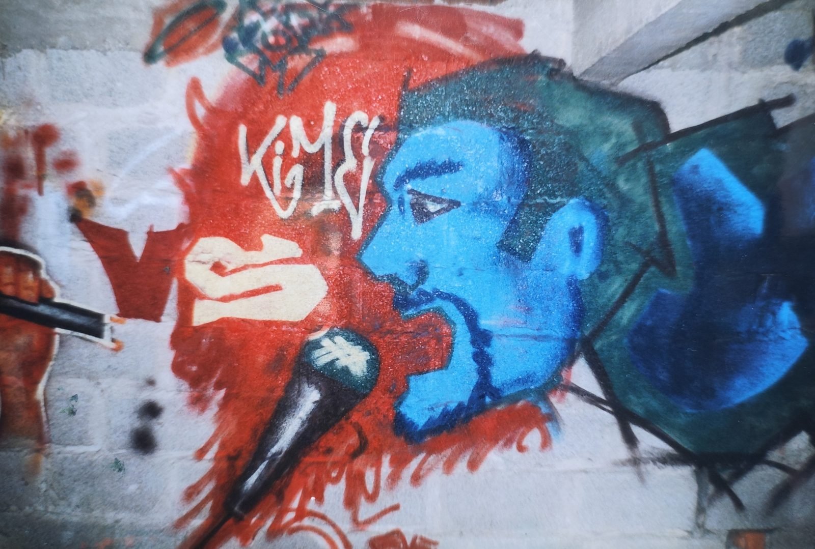 Graffiti d'un chanteur au visage bleu, micro à la bouche, sur un fond rouge peint sur un mur de parpaings.